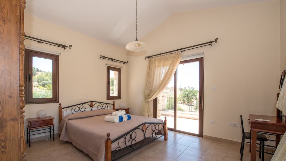 A double bedroom with iron bedstead and doors opening onto the countryside