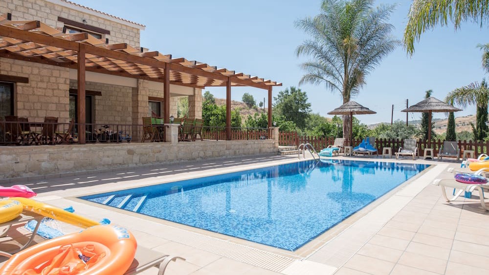 The swimming pool with palm trees and loungers beside the stone villa